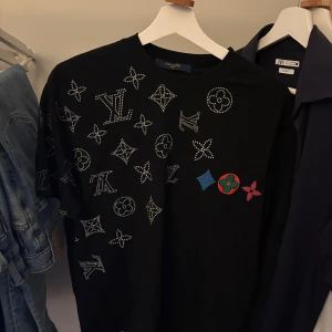 Louis Vuitton t-shirt - Svart t-shirt från Louis Vuitton med ikoniska LV-loggor och monogram. Storlek M, passar till alla stilar och tillfällen