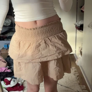 Beige volangkjol från Shein - Supersöt beige kortkjol från Shein i storlek XS. Kjolen har bred smock i midjan och dubbla volanger som ger en chill och flowig look. Perfekt för dig som gillar ljusa färger och vill ha en enkel men snygg kjol till sommaren.