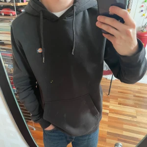 Svart hoodie från Dickies - Svart hoodie från Dickies med en liten logga på bröstet, med stor ficka. Perfekt basic-plagg i mjuk bomullsmix som funkar året runt. Plasten på snörningen har gått upp lite (sista bilden), annars nästintill helt felfri. Pris kan diskuteras 