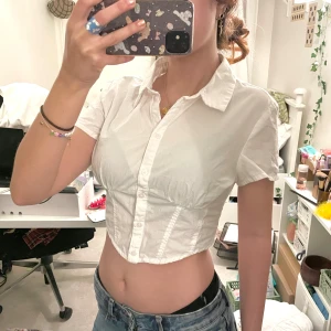 croppad skjorta - Vit croppad skjorta från H&M med snygg figurnära passform. Tillverkad i 100% bomull, jättefint skick! 🤍Kolla gärna in mina andra annonser, försöker bli av med allt så snart som möjligt 💝pris alltid förhandlingsbart, brukar gå med på de flesta prisförslag!😚