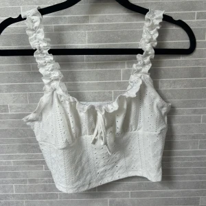 Vit linnetopp från SHEIN - Superfin vit linnetopp från SHEIN med broderade detaljer och hålmönster. Toppen har volangiga axelband, knytning framtill och är croppad. 