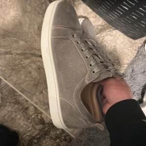 Christian louboutins - Snygga grå sneakers med vit sula och ikonisk röd undersida. Skorna har snörning och en stilren design som passar perfekt till vardags. De är tillverkade i ett material som ger en skön passform och stil.