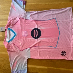 Rosa Barcelona fotbollströja Nike - Säljer en riktigt snygg Barcelona fotbollströja från Nike i rosa och ljuslila toner. Tröjan har korta ärmar, coolt grafiskt mönster och klubbmärke på bröstet. Materialet är lätt och andas, perfekt för match eller träning. Unik design med blå detaljer vid kragen.