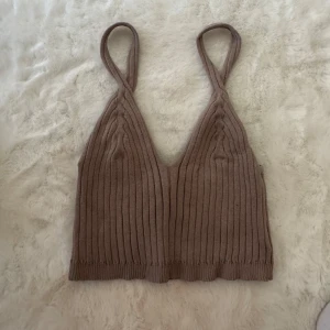 Beige ribbad stickad linnetopp H&M - Säljer en beige ribbad linnetopp från H&M i stickat material. Toppen har smala axelband och en djup v-ringning framtill. Perfekt att styla med jeans eller kjol för en chill look.