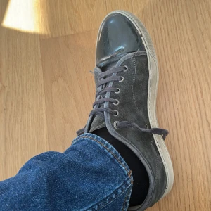 Grå mockasneakers från Lanvin - Snygga sneakers från Lanvin i grå mocka med svart lackad tå. Skorna har klassisk snörning och en stilren, rund tå. Perfekta för dig som gillar en lyxig och avslappnad look med unika detaljer.