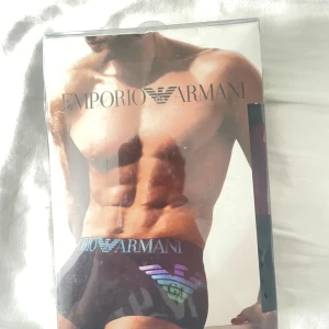 Svarta Emporio Armani kalsonger - Snygga svarta kalsonger från Emporio Armani med stretchig bomullskvalitet. De har en bred resår med logotypen i silver och ett stort, färgglatt Armani-tryck framtill. Perfekt passform och stilren design för dig som vill ha något extra.