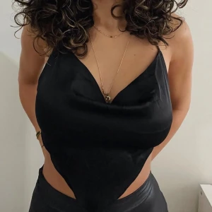 Svart satin linnetopp - Snygg svart linnetopp i satin med draperad urringning och spetsig nederkant. 