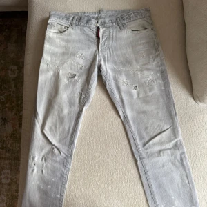 Slim grå jeans från Dsquared2 - ÄKTA Slim fit jeans från Dsquared2 i ljusgrå denim med slitna detaljer och distressed look. Klassisk femficksmodell med knappgylf och Dsquared2-logga på röd etikett. Snyggt val för dig som gillar streetstyle och italiensk design.            -                                                                                        💶Nypris: 5900
