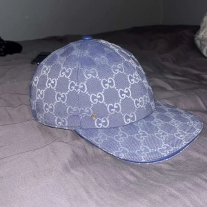 Blå Gucci keps med GG-mönster - Säljer en snygg blå keps från Gucci med det klassiska GG-mönstret över hela kepsen. Kepsen har böjd skärm och är tillverkad i jeansmaterial med insida i beige bomull. Perfekt för dig som vill ha en lyxig och trendig accessoar.