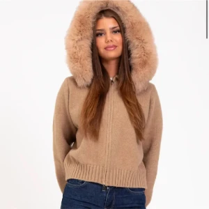 Alessa jacka Beige cardigan jacka med pälshuva - Supermysig beige cardigan jacka med fluffig pälskantad huva. Jackan är stickad med ribbade muddar och dragkedja framtill. Perfekt för kalla dagar när du vill vara både varm och snygg. Finns även i svart.pris kan diskuteras 