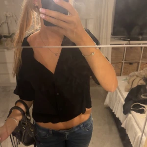 Svart blus - Säljer en svart blus med korta ärmar och v-ringad hals. Toppen har knappar framtill och en avslappnad passform💕💕