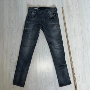 Replay Anbass svarta slim jeans - Snygga svarta Replay Anbass jeans i slim fit med klassisk femficksdesign och diskreta slitningar. Jeansen har raka ben och är tillverkade i stretchigt denim för en bekväm passform. Perfekta för dig som gillar en stilren och modern look.
