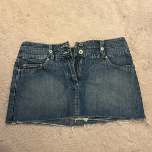 Jeanskjol med rå kant från KappAhl - Cool blå jeanskjol från KappAhl i kort modell med rå, fransig nederkant. Kjolen har klassiska fickor fram och bak, bälteshällor och dragkedja. Perfekt för dig som gillar en avslappnad och trendig stil.