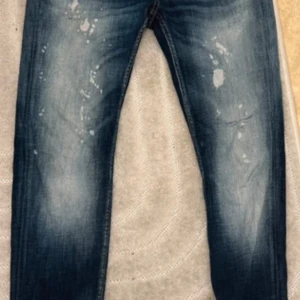 Blå jeans från Smog Denim - Snygga blå jeans från Smog Denim med coolt slitna detaljer och ljusa partier framtill. Jeansen har klassisk femficksdesign, knapp och dragkedja i gylfen samt stänkdetaljer för en trendig look. Perfekta för dig som gillar streetstyle. Fina slitningar 