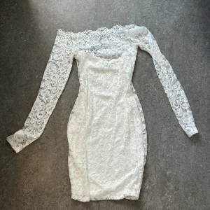 Vit spetsklänning från NLY ONE - Supersnygg vit kort spetsklänning från NLY ONE i storlek S. Offshoulder-modell med långa ärmar och vackert blommigt spetsmönster. Klänningen har en figurnära passform och romantiska detaljer längs halsringningen. Perfekt för dig som vill sticka ut med en elegant look. Klänningen är helt ny med prislapp, aldrig använd.