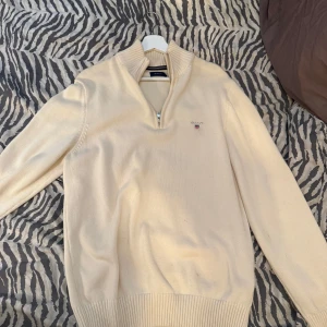 Beige stickad half zip-tröja från Gant - Snygg beige stickad tröja från Gant med halv dragkedja och hög krage. Tröjan är oanvänd och jag säljer pågrund av brist på användning. Orginal pris: 1799kr