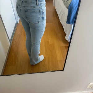 Ljusblå bootcut jeans - Säljer ett par ljusblå jeans med bootcut-modell och klassisk femficksdesign. Jeansen har normal passform och är tillverkade i mjukt denimtyg som sitter snyggt över höfterna och låren. Perfekta för dig som gillar en retroinspirerad look.