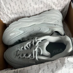 Ljusgrå chunky sneakers från FILA OANVÄNDA  - Säljer ett par ljusgrå chunky sneakers från FILA med cool vågig sula och meshdetaljer på ovandelen. . Perfekta för dig som gillar sportig och trendig stil.