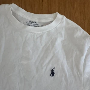 Vit t-shirt från Polo Ralph Lauren - Klassisk vit t-shirt från Polo Ralph Lauren med korta ärmar och rund hals. T-shirten har den ikoniska blå broderade loggan på bröstet och är gjord i mjuk bomull. Perfekt basic med clean look och snygg passform.