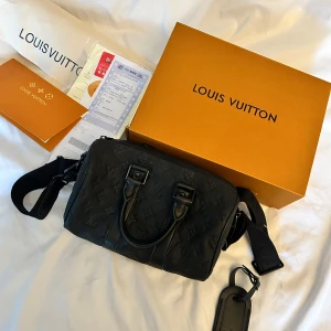 Louis Vuitton Keepall väska - Säljer en svart axelväska från Louis Vuitton med präglat monogrammönster. Väskan har både handtag och justerbar axelrem samt dragkedja upptill. Tillbehör som tag och originalkartong medföljer. Perfekt för dig som vill ha en stilren och lyxig accessoar.