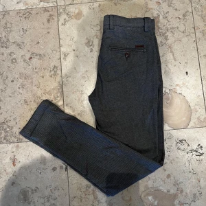 Grå Slim Fit Chinos från Jack & Jones - Snygga grå kostymbyxor från Jack & Jones, modell Slim/Marco. Byxorna har smal passform, bälteshällor och bakfickor med knapp. Perfekta för en stilren look. Byxorna har använts en gång. Nypris 600kr, mitt pris 200kr.