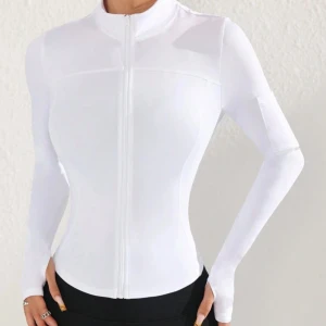 Vit tight ziptröja med lång ärm - Säljer en vit, tight ziptröja med lång ärm och hög krage. Tröjan har dragkedja framtill som kan öppnas hela vägen och är tillverkad i ett stretchigt material. Den har även en ficka på armen man kan lägga mobilen i. Perfekt för en sportig och stilren look.