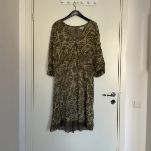 Beige blommig klänning från Noa Noa - Säljer en beige blommig klänning från Noa Noa i storlek XL. Klänningen har trekvartsärm och har en omlottliknande v-ringning. Perfekt för dig som gillar en avslappnad men stilren look.