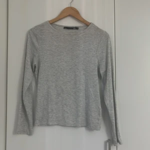 Ljusgrå långärmad tröja från 157 - En enkel och stilren ljusgrå långärmad tröja från 157. Tröjan har rund halsringning och är tillverkad i ett mjukt bomullsliknande material. Perfekt basplagg att ha i garderoben.