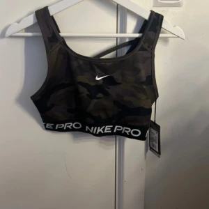 Nike Pro sport-bh med camomönster - Säljer en Nike Pro sport-bh i svart och grönt camomönster. Bh:n har bred resår med Nike Pro-logga och korsade axelband i ryggen. Tillverkad i Dri-Fit material som andas och passar perfekt till träning . Helt ny nytt pris är 379kr