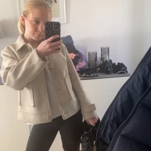 Beige ulljacka med knappar - Snygg beige jacka i ullblandning med klassisk krage och stora knappar framtill. Jackan har raka linjer, två fickor och är lätt att matcha till olika outfits. Perfekt för dig som gillar stilrena och tidlösa plagg. Den har dock ett hål under armen så säljer ganska billigt