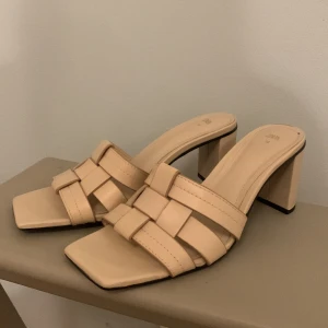 Beige skor med klack från Zara - Säljer ett par stilrena beige sandaler från Zara med flätade remmar. Skorna har en bred klack och öppen design, perfekta för varmare dagar. Snyggt och trendigt val till sommaren! Passar till flera outfits! 
