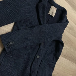 Mörkblå kavaj från Zara Boys - Säljer en mörkblå kavaj från Zara Boys med två knappar framtill och två fickor. Kavajen har lång ärm och klassisk krage, perfekt för en dressad look. Materialet har en lätt textur som ger en snygg känsla.