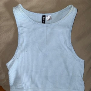 Ljusblå ribbad croppad linnetopp - Säljer en ljusblå croppad linnetopp från H&M. Toppen är ribbad och ärmlös med rund halsringning. Perfekt för varma dagar och enkel att matcha med olika outfits.