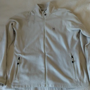 Vit fleecetröja från Haglöfs - Säljer en vit fleecetröja från Haglöfs med hel dragkedja och två fickor framtill. Tröjab har hög krage och diskret logga på bröstet. Perfekt för lager-på-lager och outdoor. I mycket gott skick.