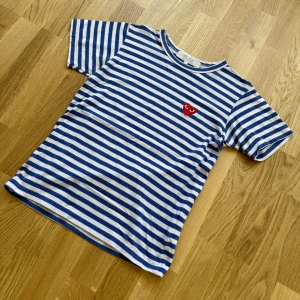 Randig t-shirt från Comme des Garçons Play size S  - Blåvit randig t-shirt från Comme des Garçons Play med det ikoniska röda hjärtat broderat på bröstet. Klassisk passform och rund halsringning. Perfekt för en stilren och trendig look.