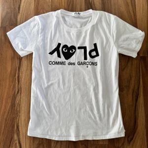 Comme des Garçons Play (cdg) tshirt - Vit t-shirt med svart tryck och ikoniskt hjärta från Comme des Garçons Play. Klassisk rund hals och korta ärmar. Tillverkad i 100% ull, med PLAY-logga och text framtill. Hör av dit vid funderingar så löser vi en deal