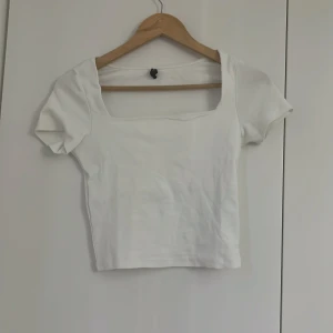 Vit croppad topp med fyrkantig ringning - Säljer en vit croppad topp med korta ärmar och snygg fyrkantig ringning magtröja. Perfekt till jeans eller kjol för en stilren look. Enkel och trendig design som passar till många tillfällen. 