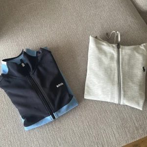 Två zipjackor från Boss och Polo Ralph Lauren - Två snygga zipjackor, en i svart och ljusblå från Boss och en i ljusgrå från Polo Ralph Lauren. Båda har dragkedja framtill och hög krage. 