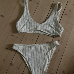 Vit och blårandig bikini - Säljer en bikini i vitt med tunna blå och svarta ränder. Bikinin har en sportig topp med breda axelband och höga trosor. Materialet är strukturerat och känns lite tjockare än vanligt. Super fin men passar inte, lappparna är borta men skulle säga 36/38 i storlek