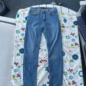 Ljusblå jeans från Nudie Jeans - Säljer ett par klassiska ljusblå jeans från Nudie Jeans med fem fickor och orangea sömmar. Jeansen har normal passform och raka ben. Perfekta för en avslappnad stil och passar till det mesta.