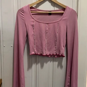Rosa croppad långärmad topp från SHEIN - Trendig rosa croppad topp från SHEIN med långa ärmar och vågig kant nertill. Toppen har dekorativa sömmar framtill och en rundad urringning. 
