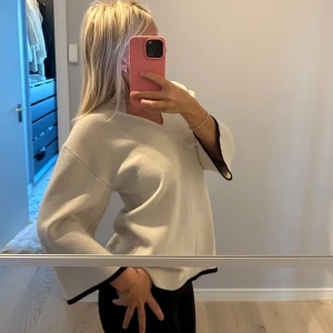 Vit v-ringad tröja med vida ärmar - Säljer en vit v-ringad tröja med vida trekvartsärmar och svarta detaljer vid ärmslut och nederkant. Tröjan har en lös passform och är perfekt för en stilren look.