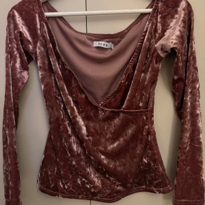 Rosa sammetsblus från NA-KD - Säljer en glansig rosa sammetsblus från NA-KD med omlott-design och djup v-ringning. Blusen har långa ärmar och en figurnära passform. Använd vid två tillfällen! 