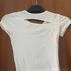 Vit ribbad topp med cut out från Gina Tricot - Säljer en vit ribbad topp från Gina Tricot i storlek XS. Toppen har korta ärmar och en snygg cut out-detalj vid halsen som ger en cool look. Perfekt till jeans eller kjol!Frakt tillkommer