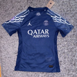 PSG x Jordan 24/25 player version fotbollströja - HELT NY! Aldrig använt med tags! Säljer en blå Paris Saint-Germain fotbollströja i samarbete med Jordan. Tröjan har vita detaljer, PSG-logga på bröstet, Qatar Airways som sponsor och ett mönster på axlarna. Kortärmad modell i lätt och ventilerande material. 