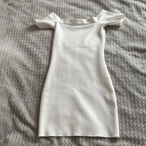 Vit offshoulder klänning - Säljer en stilren vit offshoulder klänning med tight passform. Klänningen är kort och har en minimalistisk design utan mönster eller extra detaljer. Perfekt för dig som gillar en enkel och elegant look. Den är aldrig använd och är från Zara. Hade sagt den sitter som xs-s