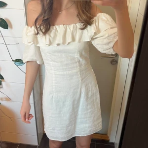 Vit offshoulder klänning med volang - Superfin vit klänning från hm i storlek 34 / XS. Klänningen är i linne med offshoulder-modell och volang upptill. Klänningen har korta puffärmar och en figurnära passform. Har en dragkedja i sidan som gör det lättare att ta på o av den💕💕
