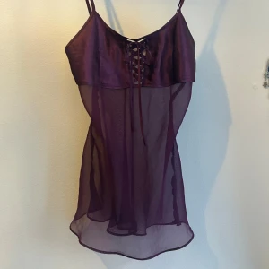 y2k avant garde 00s 2000s camisole topp babydoll - BABYDOLL-TOPP I LILA MESH MED SNÖRNING🪁 Unik och avantgarde-inspirerad 00-tals camisole/babydoll-top i djup plommonlila nyans. Överdelen är i glansigt satinliknande tyg med dekorativ snörning framtill, medan underdelen är i transparent mesh som faller vackert över kroppen. Smala justerbara axelband. Storlek: Ingen märkning - passar bäst storlek S-M och B-C kupa