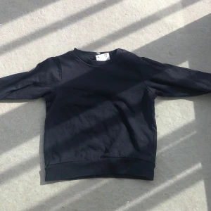 Svart sweatshirt med rund hals - En basic svart sweatshirt med rund hals och långa ärmar. Tröjan har ribbade muddar vid ärmslut och nederkant. Perfekt för en enkel och stilren look.