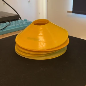 Gula markeringskoner för fotbollsträning - Säljer ett gäng gula markeringskoner som är perfekta för fotbollsträning eller övningar på planen. Tillverkade i plast och enkla att stapla och ta med sig. Perfekt för att markera ytor eller göra hinderbanor.